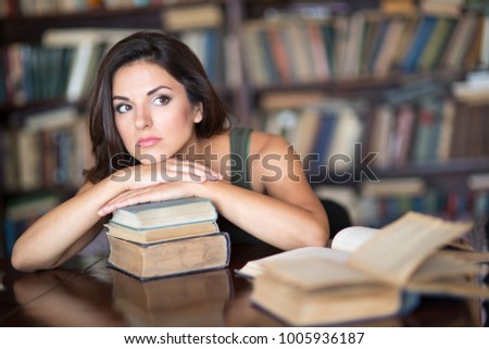 Beautiful young female student sitting on the background of bookshelves in the library 