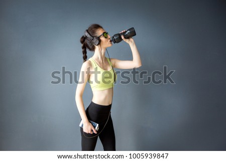 The young girl trainer drinks a sports drink to enhance the body's tone