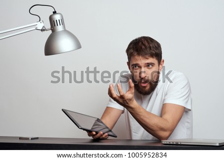   surprised man with a tablet sitting at a table, a lamp                             