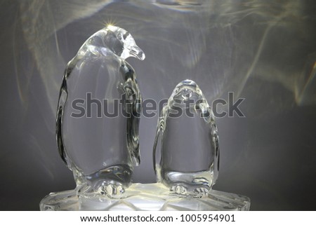 Transparent Glass Sculpture Of Two Penguins Lit From Underneath, Reflecting Pattern Light On To Background