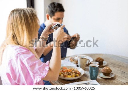 Woman sitting in the restaurant with her boyfriend taking pictures of the food with mobile phone