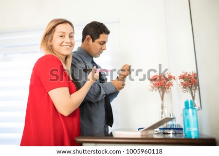 Portrait of pretty young woman putting on makeup with her husband buttoning the sleeves