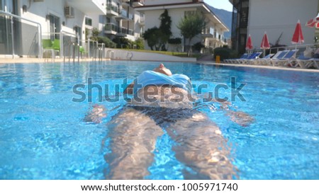 Young beautiful girl relaxing in pool at warm sunny day. Woman swimming on the back. Summer vacation holiday concept. Slow motion.