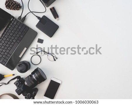 top view of photographer concept with digital camera, battery charger camera, memory card storage box, external harddisk, flash, notebook and camera accessory on white background with copy space.