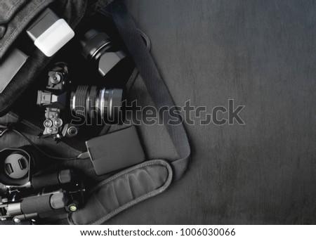 top view of photographer concept with digital camera, external harddisk, flash, notebook and camera accessory on camera bag on black background with copy space.