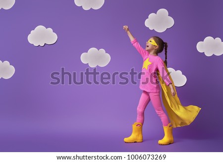 Little child is playing superhero. Kid on the background of bright ultra violet wall. Girl power concept. Yellow, pink and  purple colors.                  