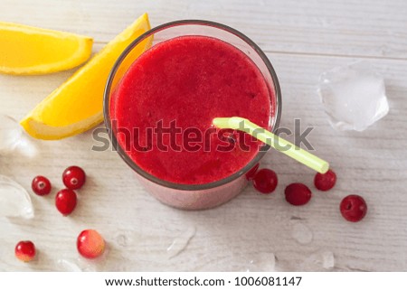 Glass of red smoothie from cranberry and orange with straw and ice on wooden background, well being weight loss concept, berry smoothie with ingredients, summer dessert for healthy lifestyle, top view
