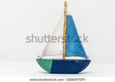 A wooden toy yacht. The toy boat shows signs of use, but the sails are in tact and still attached to the wooden mast. It is painted in 4 colours with a simple keel indicating this toy is ornamental.