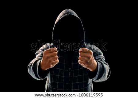 Silhouette of a man in a hood on a black background, his face is not visible, showing a fist in the camera. The concept of a criminal, incognito, mystery, secrecy, anonymity.
