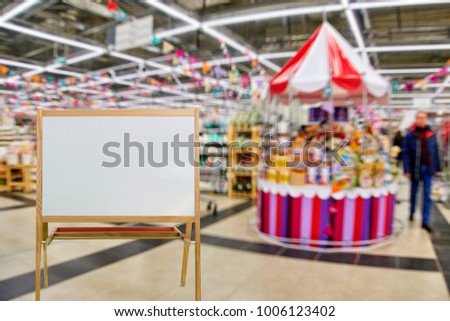 Chalkboard in wooden frame as place for your text on the foreground. Department of gifts, shelves with souvenirs, out of focus, blurred, in the background.