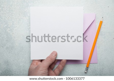 A square layout of paper and a pink envelope in his hand.