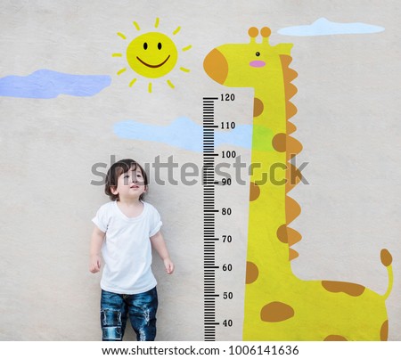 Closeup asian kid stand for measure height and look at cute giraffe cartoon at the marble stone wall textured background