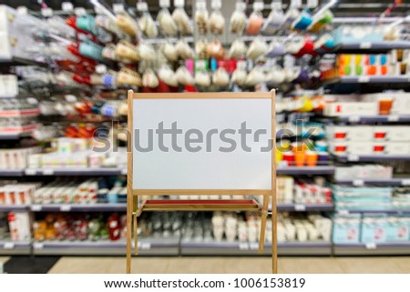 Chalkboard in wooden frame as place for your text on the foreground.   The department of dishes, shelves and racks with plates, mugs, vases, out of focus, blurred, in the background.