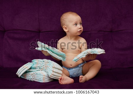 Little boy with stack of diapers or nappies on purple sofa background Royalty-Free Stock Photo #1006167043