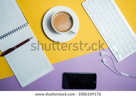 A modern office with a computer, a smartphone with a black screen on a laptop and a cup of coffee. Top view with a copy, keyboard and camera for headphones. isolated on a yellow background