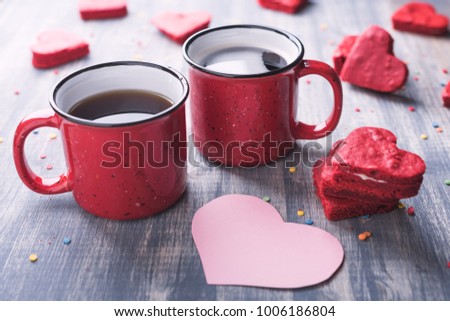 Two cups of coffee on wooden background. Red velvet heart shape cookies on table. Vintage and retro toned. Pink note. 