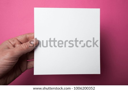 Mockup square empty white paper holds in hand. Isolated on a pink background.