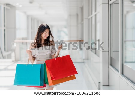 Beautiful young happy Asian woman with colorful shopping bag using smartphone while shopping in mall Royalty-Free Stock Photo #1006211686