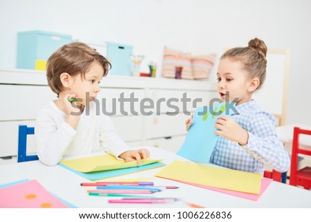 Little girl showing her drawing to elementary schoolboy and telling him its idea