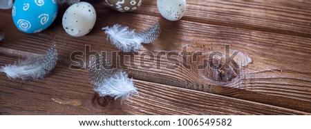 Painted Easter eggs with feathers and a branch of sakura on a dark wooden background, border design panoramic banner 