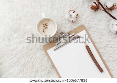 Flat lay, top view female cozy table desk with clipboard, coffee and cotton on white sheepskin rug. Blogger concept 