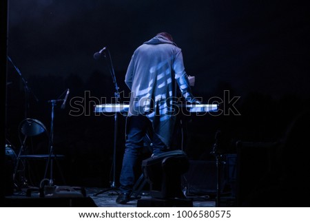 Male musician plays a musical instrument on the stage. Artist playing on the keyboard synthesizer piano keys. Live concert of electronic music at night in summer festival. Colorful, abstract lights.