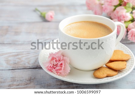Cup of fresh morning coffee with pink carnation flowers on a wooden background. Valentine's day concept.