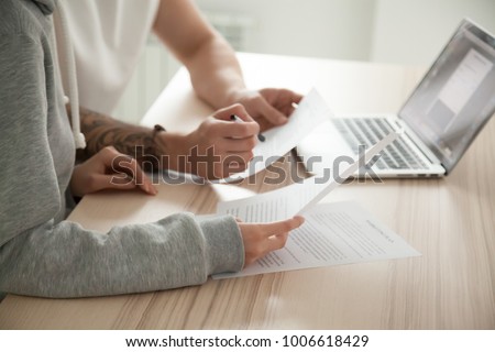 Couple reading legal documents at home with laptop, family considering mortgage loan or insurance, studying contract details, discussing terms and conditions, close up view of hands holding papers