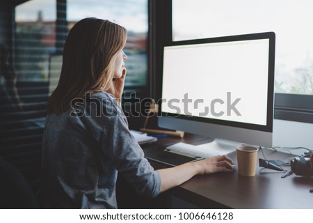view from back to female student is talking on smartphone sitting at desk in front of monitor with blank space for design. Mockup screen with copy space. woman makes a business call