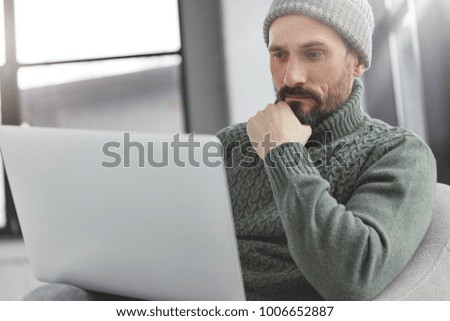 Confident bearded office manager watches database on modern laptop computer, reads something with serious concentrated expression. Successful financier sends messages, thinks about designing startup