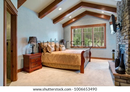 Chic master bedroom: vaulted ceiling with wooden beams over the wood sleigh bed facing stone wall fireplace. Northwest, USA