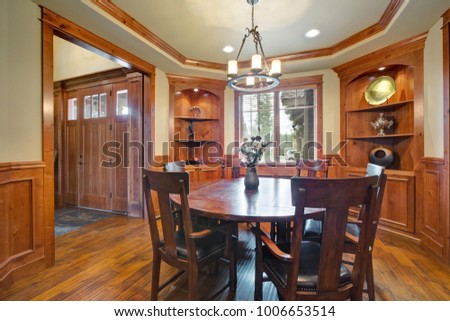 Elegant dining room with built-in shelves, round dining table with leather chairs, ivory batten and board paneled walls and hardwood floor. The room is connected to the entrance hall.  Northwest, USA