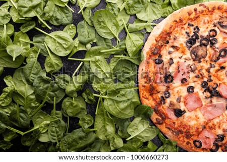Delicious pizza next to spinach on dark wooden table