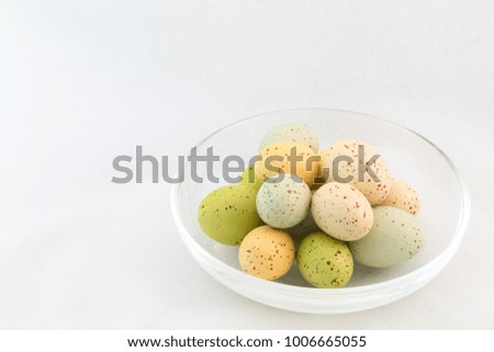 Glass bowl with group of multicolored speckled eggs; right side; white background