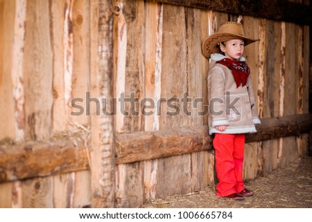 a little girl in a cowboy hat stands near the wall of a barn