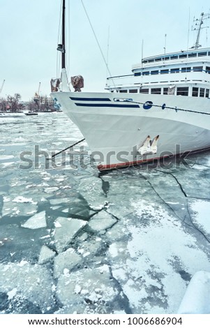 A white blue passenger ship anchored in a frozen river covered with ice and snow