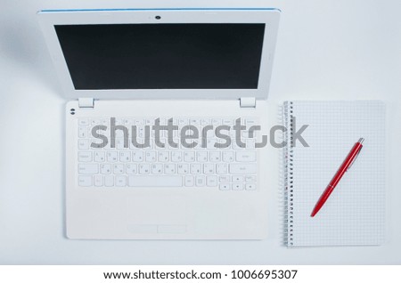 White notebook with a red pen and a laptop for business work
