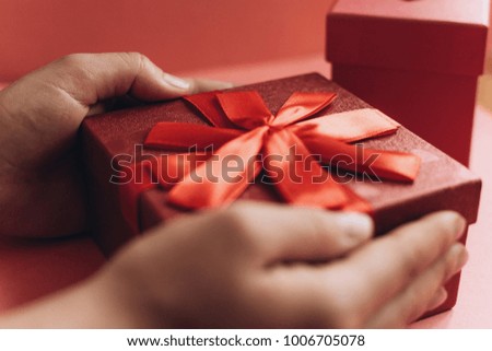 The girl has received a gift in a beautiful red box with a ribbon and is going to open it.