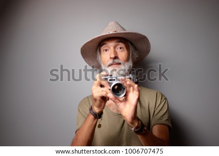 Traveler and photographer. Studio portrait of handsome senior man with gray beard and hat holding photocamera.