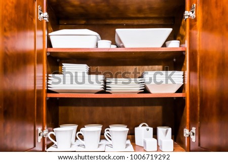 Open wooden kitchen cabinet door cupboard with many white dishes, plates, cups on shelves closeup Royalty-Free Stock Photo #1006719292
