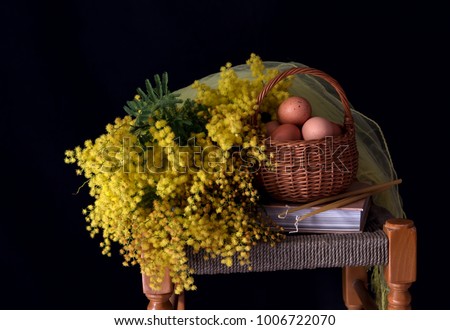 The easter still life. Eggs in a wicker basket, a bouquet of mimosa and church candles on wooden stool close-up.