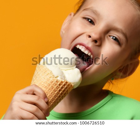 Pretty baby girl kid eating licking vanilla ice cream in waffles cone on yellow background