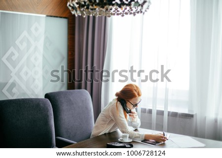 redhead businesswoman working in a office with tablet and talking on phone