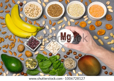 Food rich in magnesium (Mg). Various natural sources of vitamins. Useful food for health and balanced diet. Prevention of avitaminosis. Man's hand holds tag with name of magnesium. Top view
