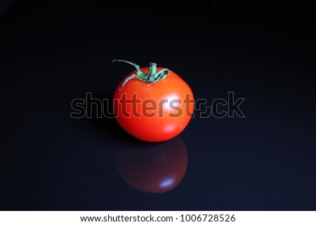 Tomato. Red mini whole tomato on black reflective studio background. Isolated black shiny mirror mirrored background for every concept.