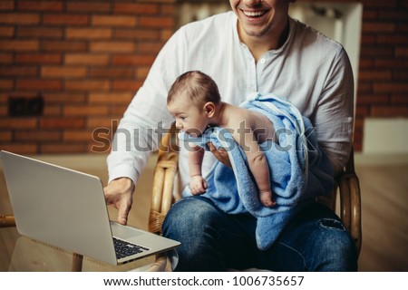 Father With Newborn Baby Working From Home office Using Laptop