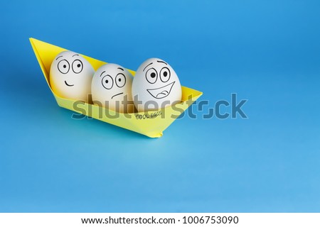 Funny eggs with drawn faces float on the ship. Three white eggs in a yellow paper boat on a blue background. Easter and travel concept.