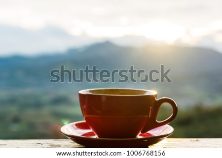 A red cup of hot latte on wood table with mountain background