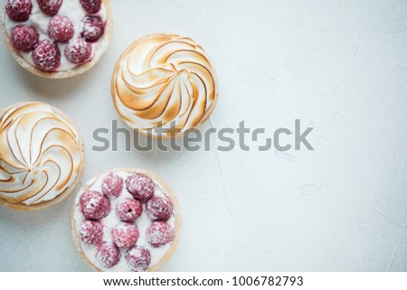 Delicious lemon and raspberry tartlets with meringue on a white vintage plate. Sweet treat on a light blue background. Flat lay and copy space. Top view