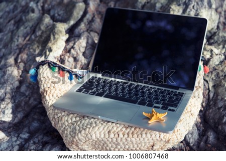 Business and technology with nature in vacation concept. Empty laptop screen put on summer traveling bag on the beach. Nomad or freelance. Picture for add text message. Backdrop for design art work.